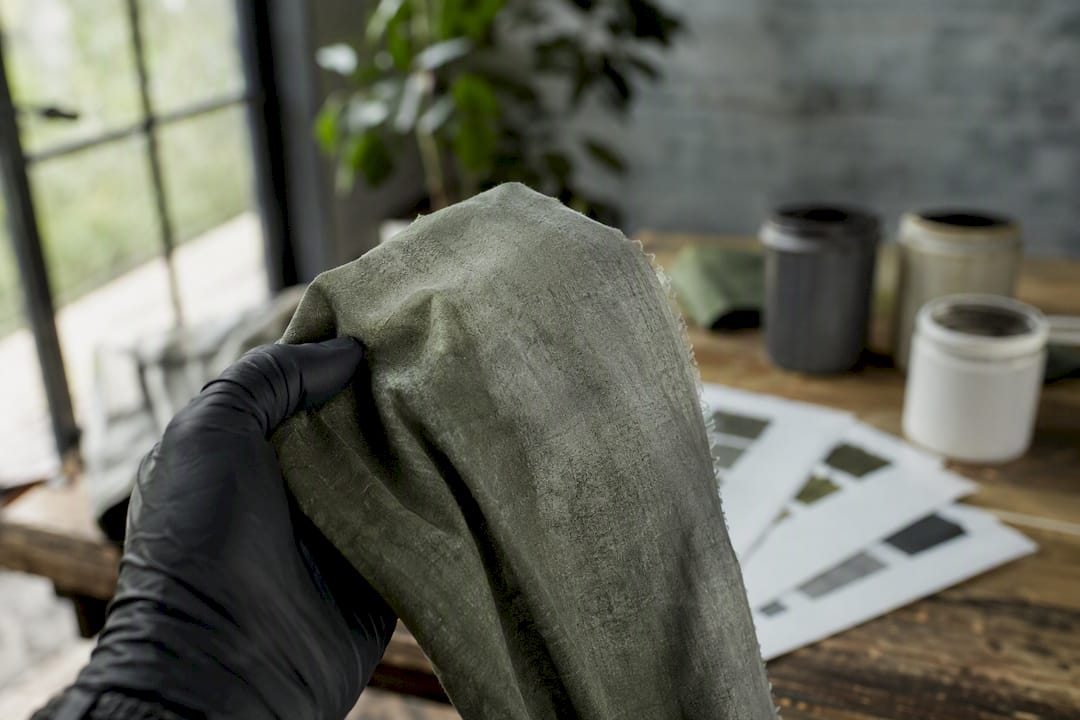 Mit Handschuhen wird ein gefärbtes Stoffmuster im Labor begutachtet