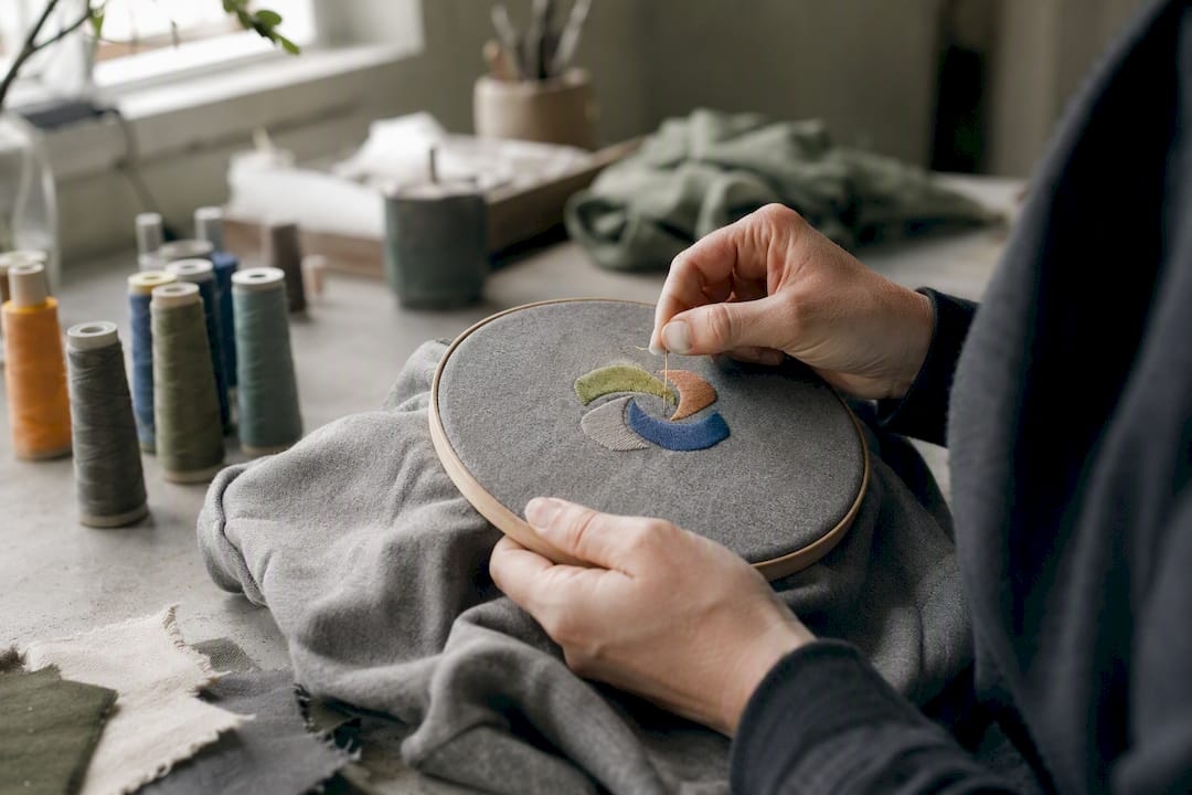 Detailaufnahme: Mit viel Liebe stickt eine Hand ein nachhaltiges Hoodie-Unikat.