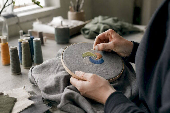 Detailaufnahme: Mit viel Liebe stickt eine Hand ein nachhaltiges Hoodie-Unikat.